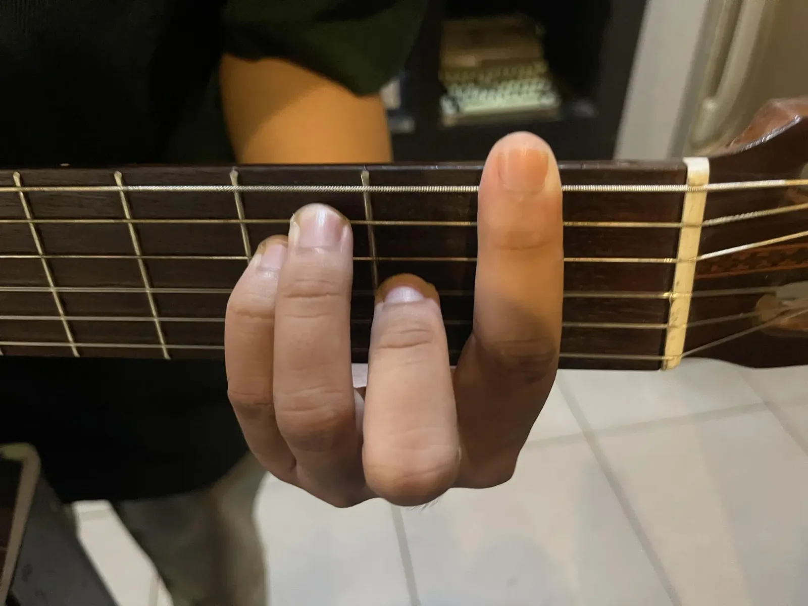 Ảnh chụp bàn tay trái bấm thế chặn F trên cần đàn guitar, ngón trỏ nằm ngang đè qua cả sáu dây ở ngăn 1, ba ngón còn lại bấm từng dây riêng